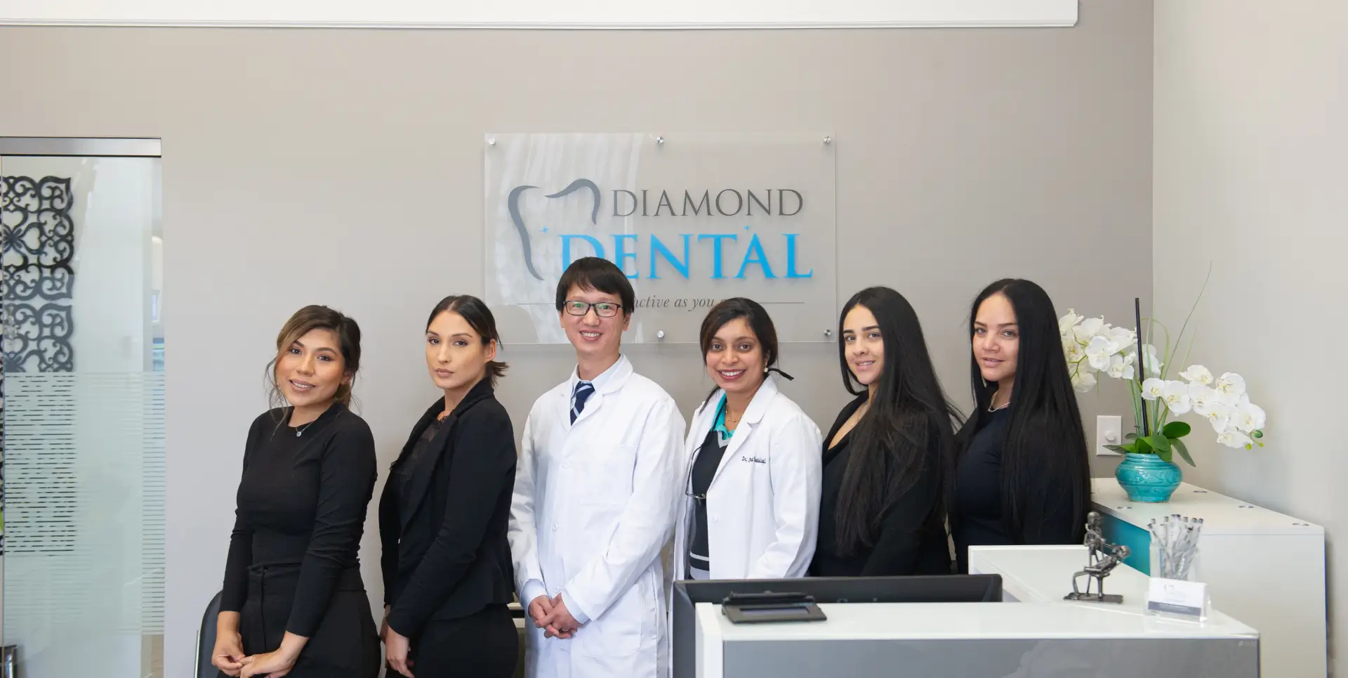 A dental team, including two dentists, poses together in front of a sign reading "Diamond Dental."