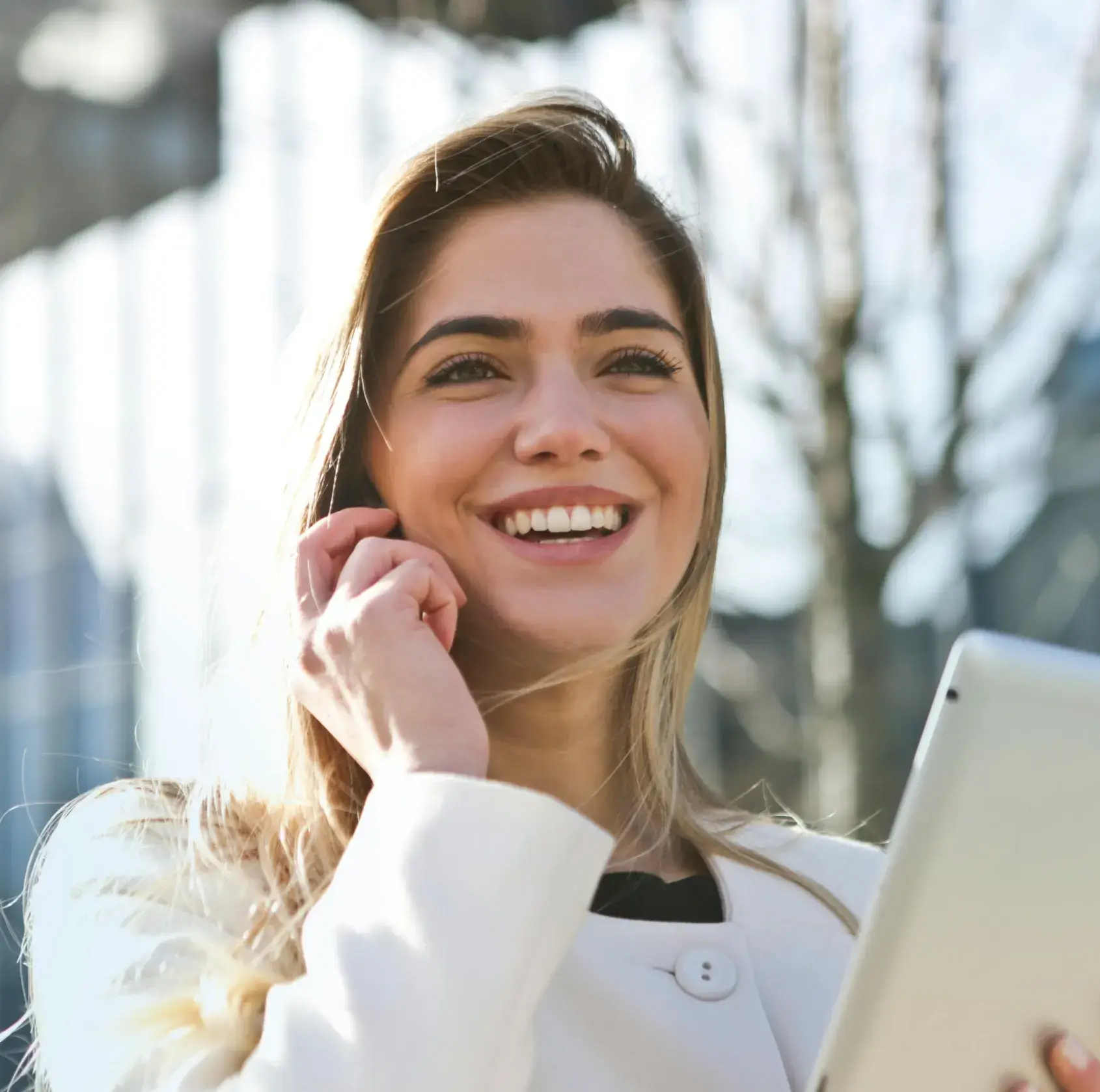 A woman smiling while talking on a phone and holding a tablet.