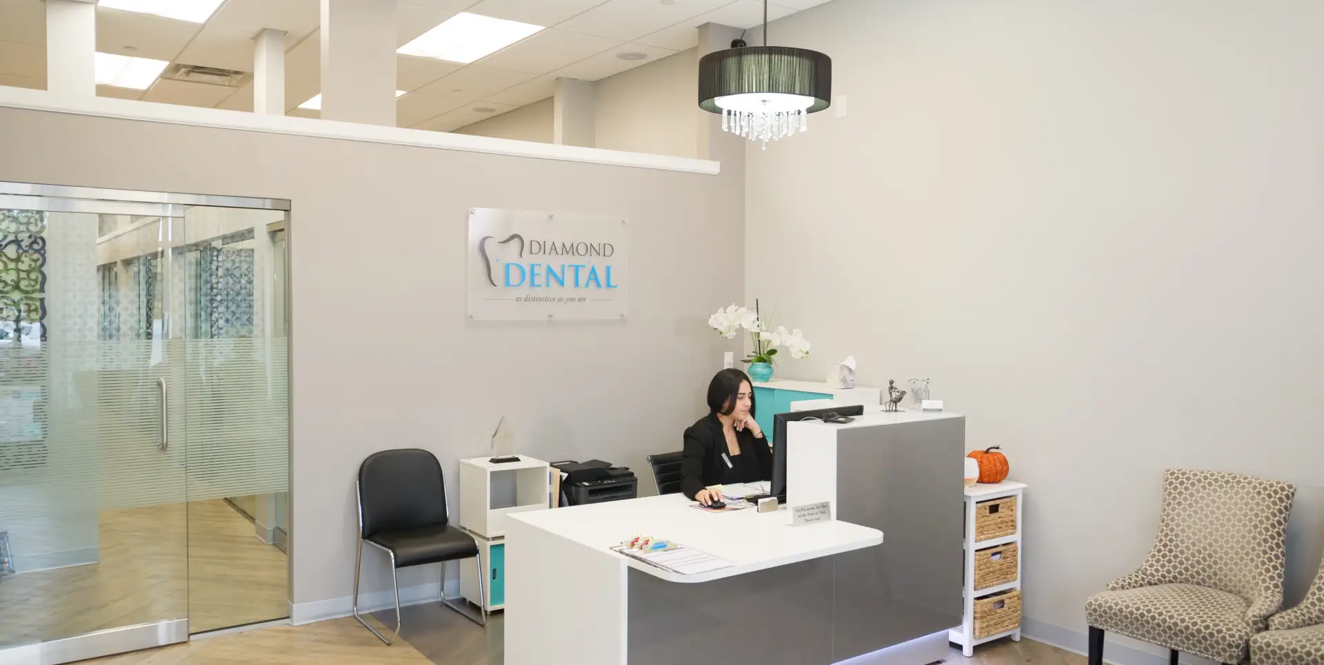 A woman sits at a reception desk in a dental office, speaking on the phone.