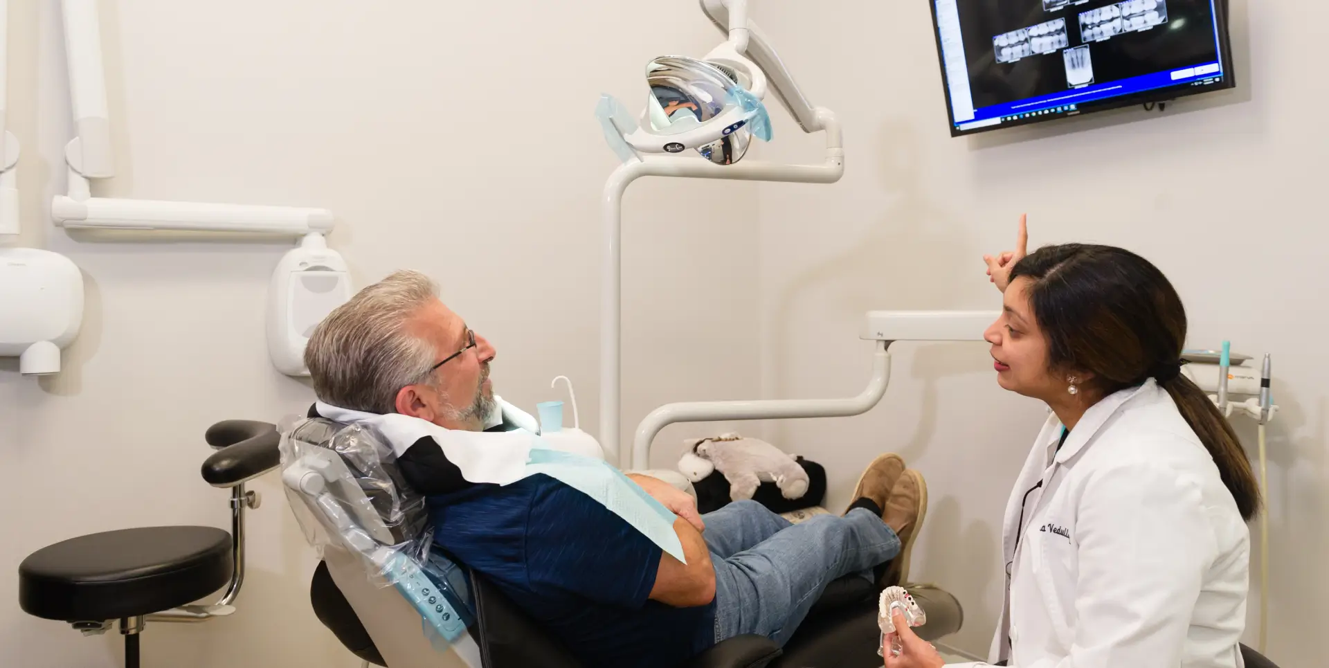 A dentist explains an X-ray to a patient seated in a dental chair.