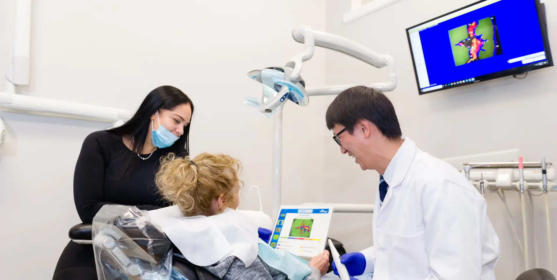 A dentist shows a young patient dental images on a screen while a woman observes.