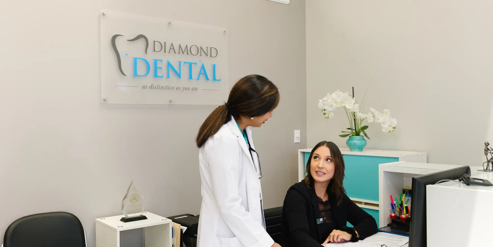 A dentist talks to a receptionist at the front desk of a dental office.